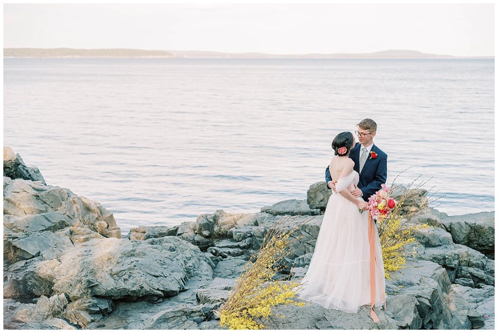 wide shot of bride and groom posing on beach in Maine