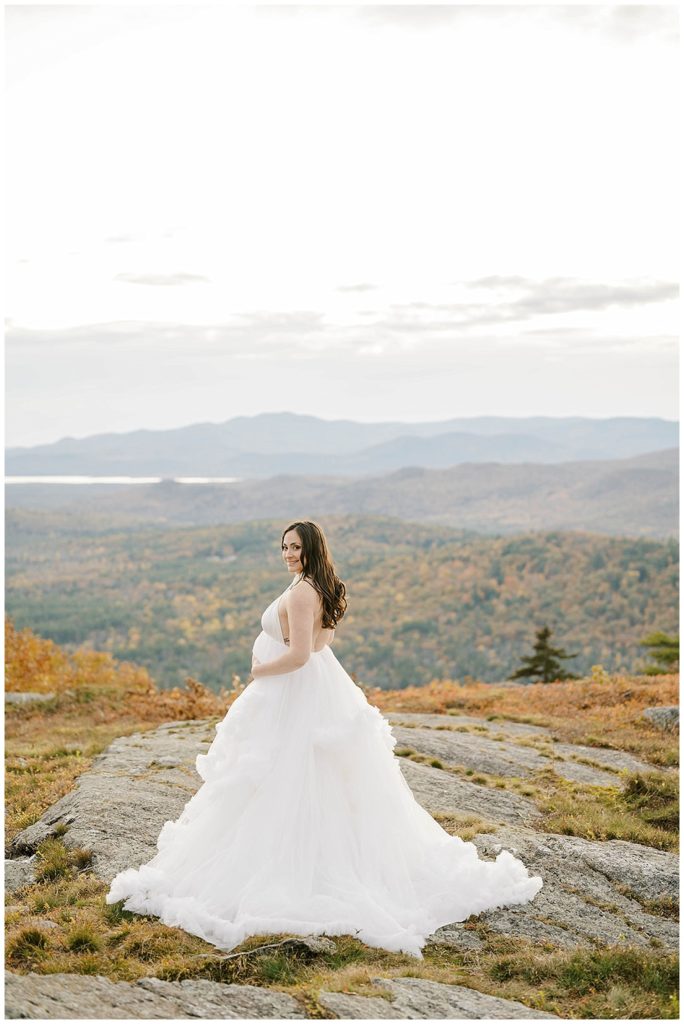mom to be looking back at camera in white ruffle dress on Foss Mountain