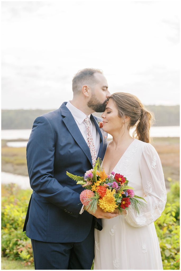 groom kissing the bride's forehead during couple photos in Maine