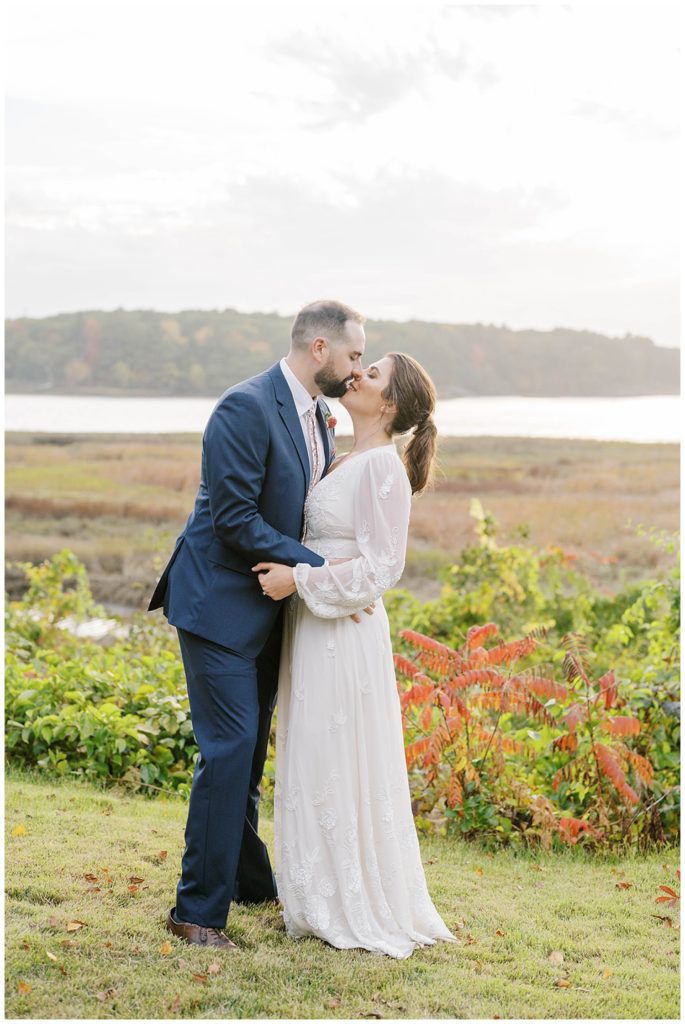 groom kissing the bride outside near the ocean in Maine