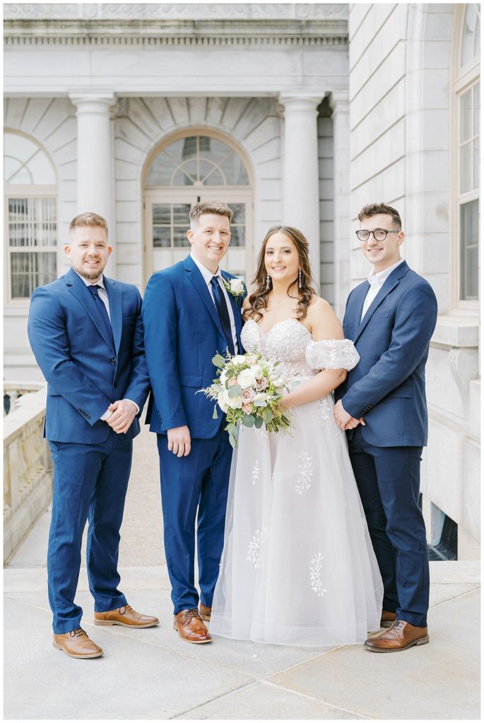 bride posing with groom and groomsmen outside Portland City Hall