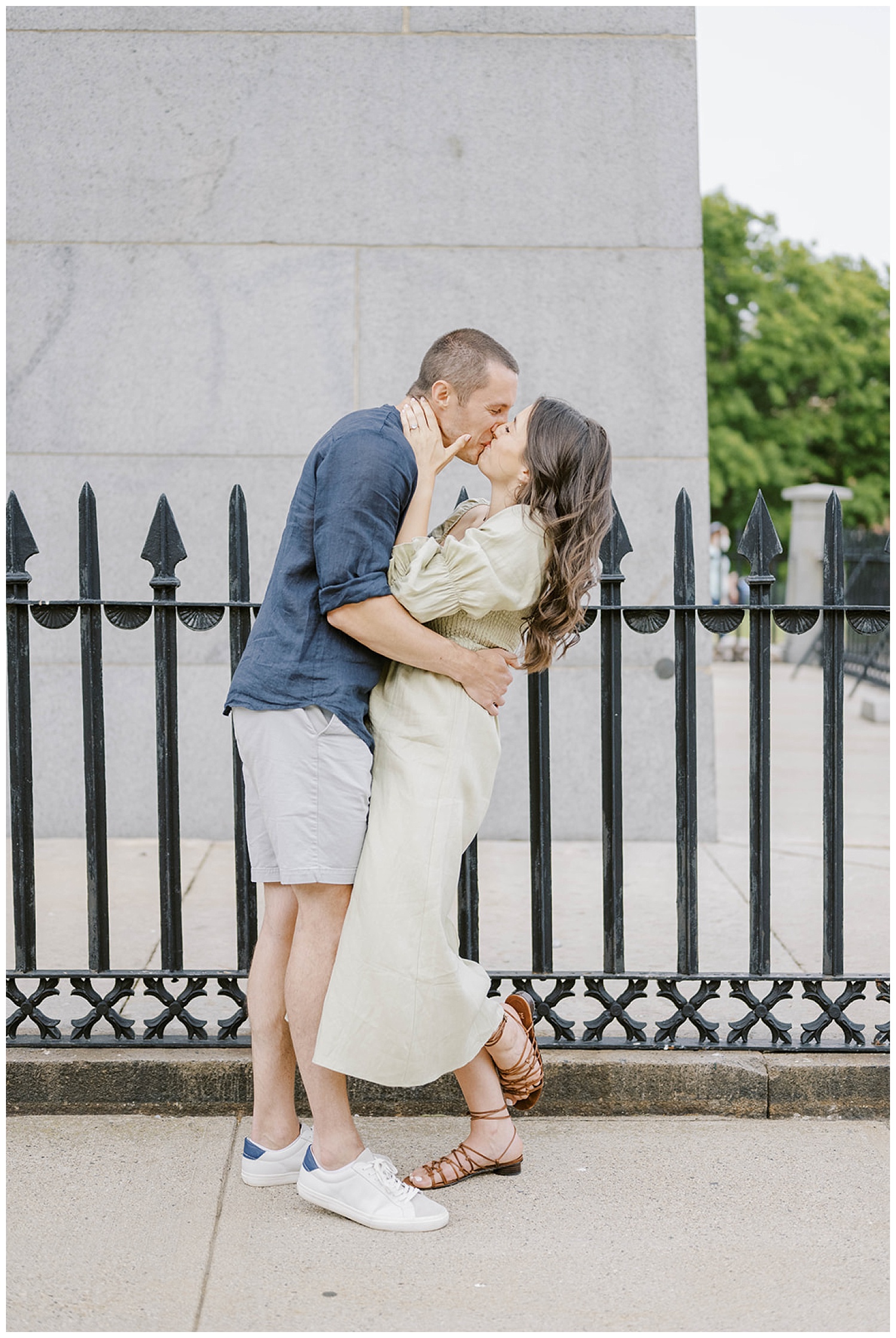 engaged couple kissing in front of black fence at Monument Square in Boston