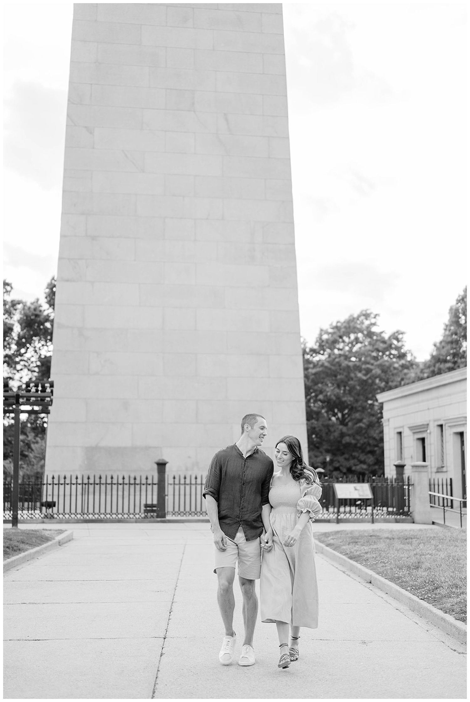 engaged couple walking together in front of Monument Square in Boston
