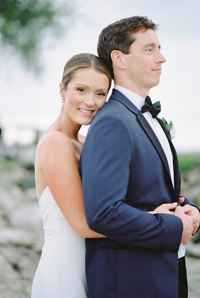 bride embraces groom from behind with her cheek on his shoulder