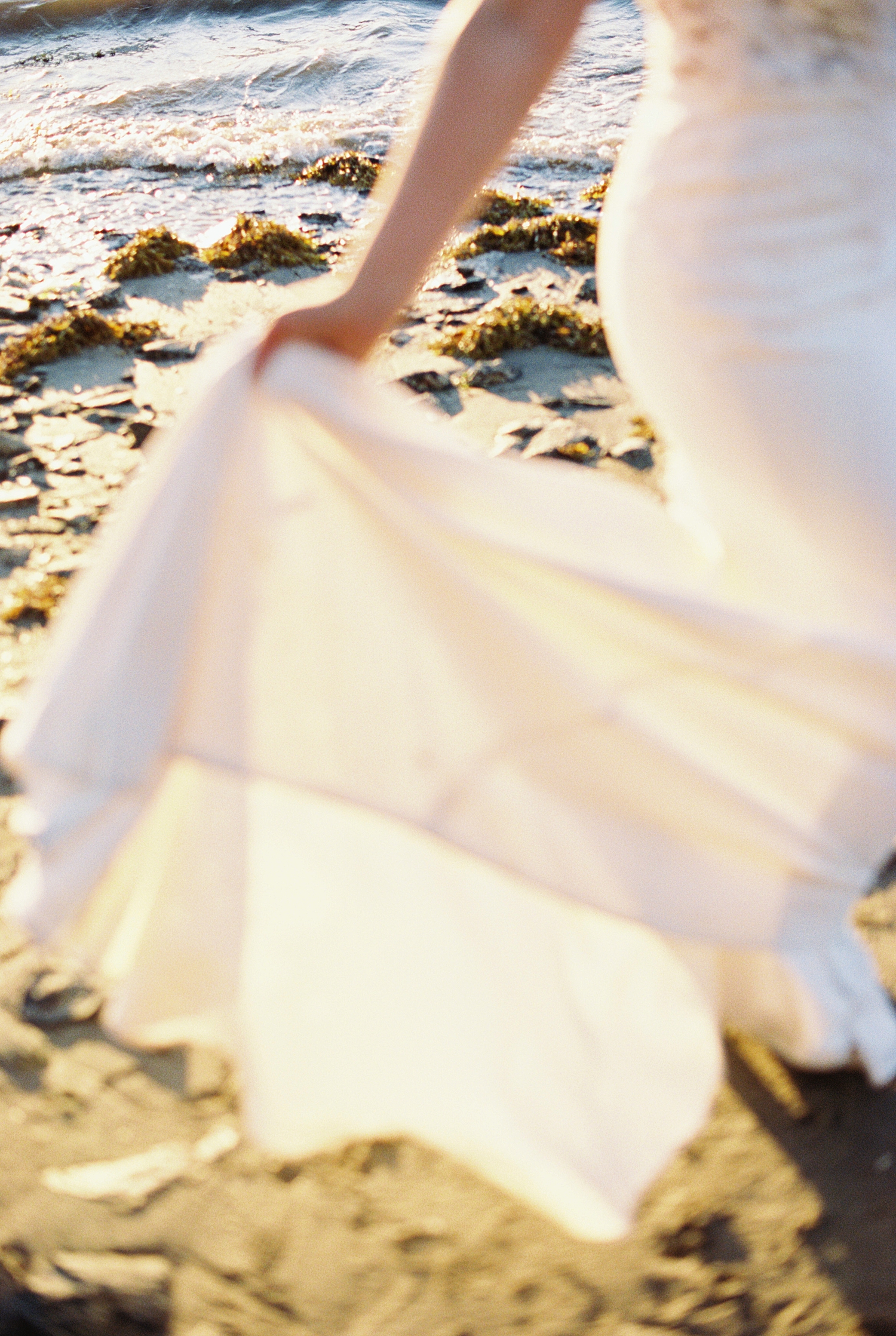 bride holds dress train while talking on New England beach during wedding portraits