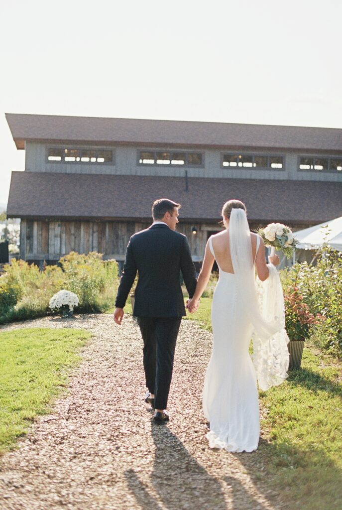 couple walks toward barn for wedding reception