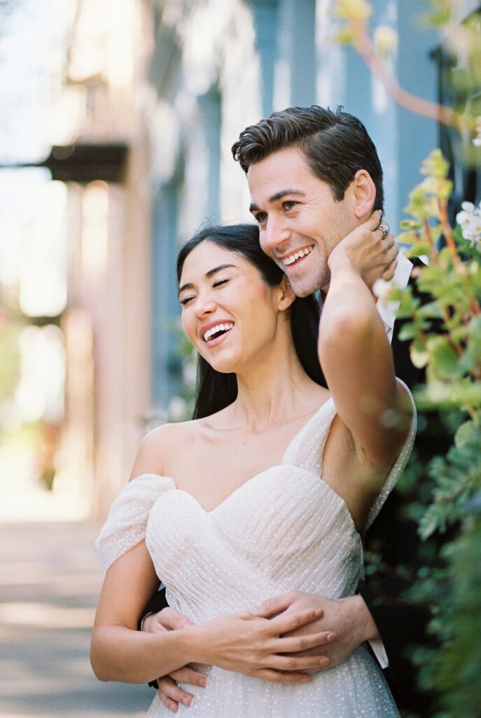 bride reaches back to touch the groom's face as he holds her from behind