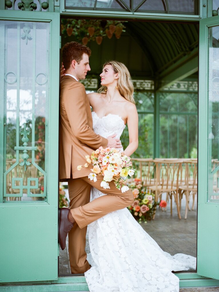 groom in a brown suit leans on a green building door with bride