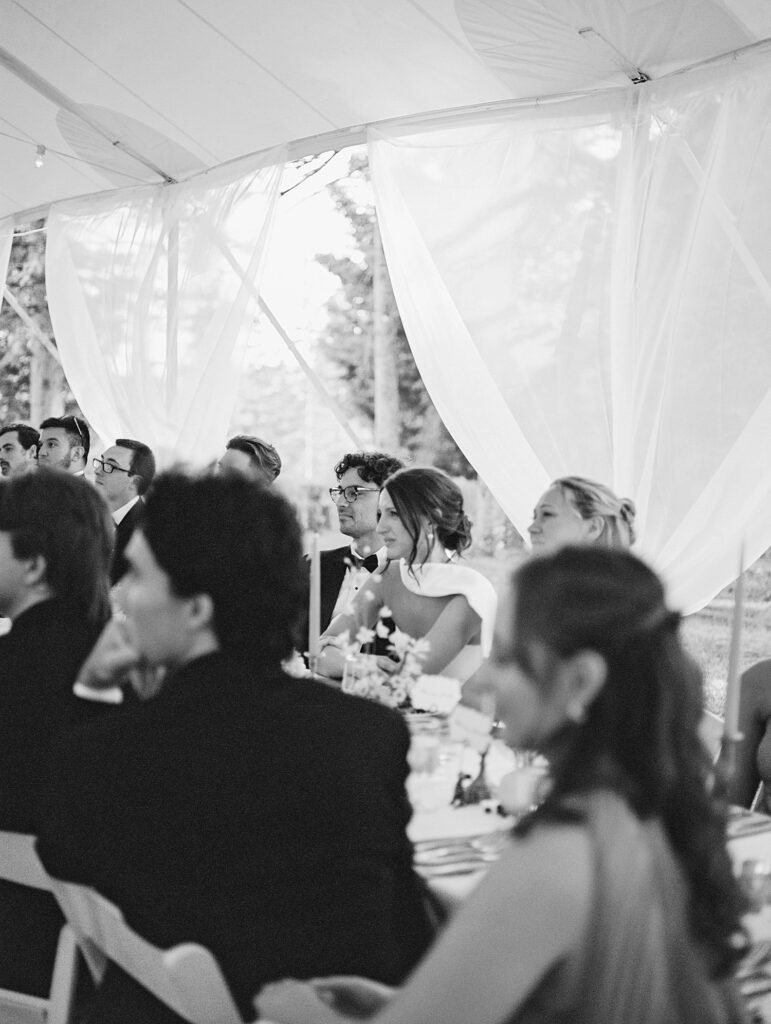 couple listen to speeches during tented wedding reception