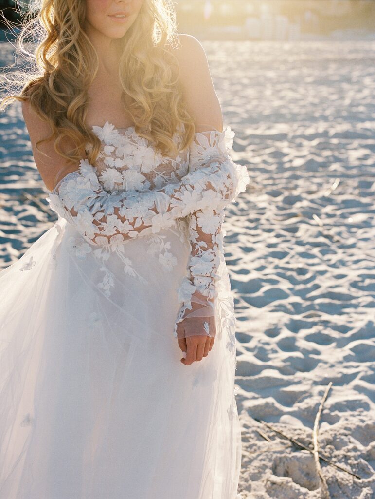 close up of floral appliqué detail on bridal gown on a beach