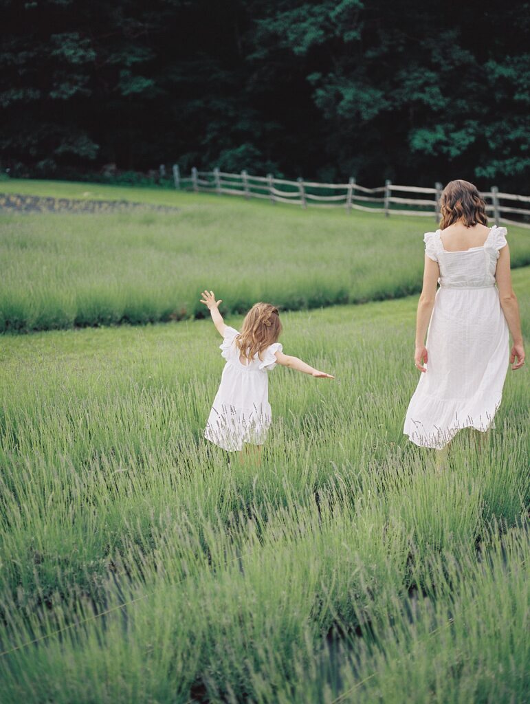 mother and daughter walk through a field with their backs to the camera