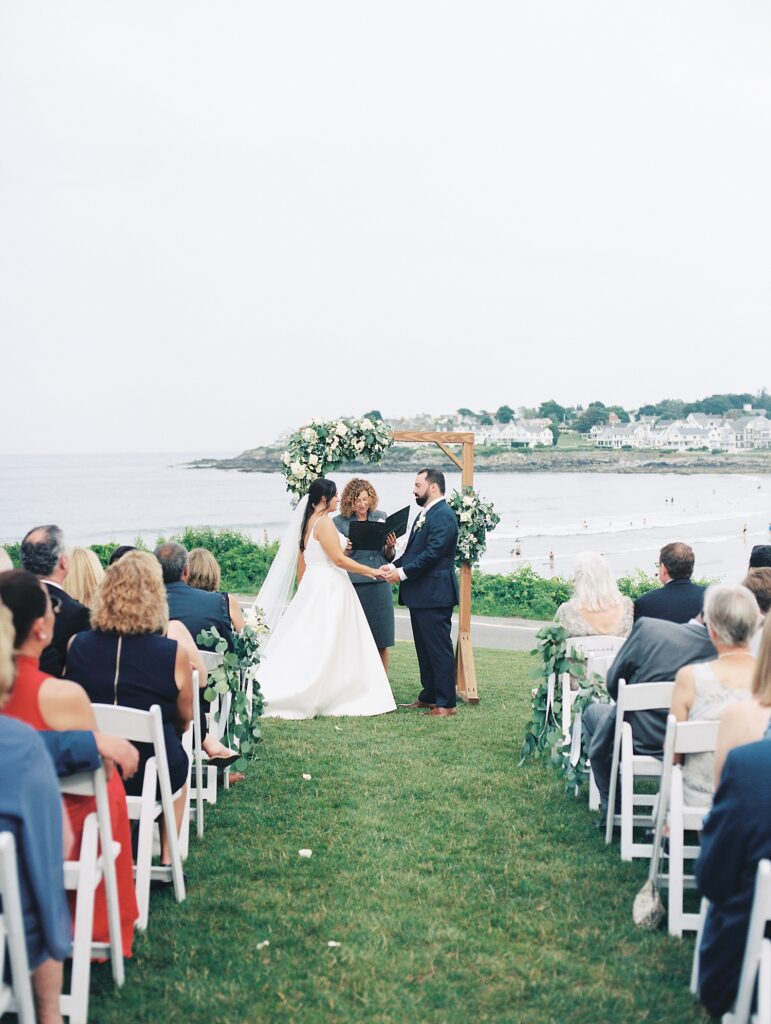 couple stand together under a wooden arch with flowers during wedding ceremony