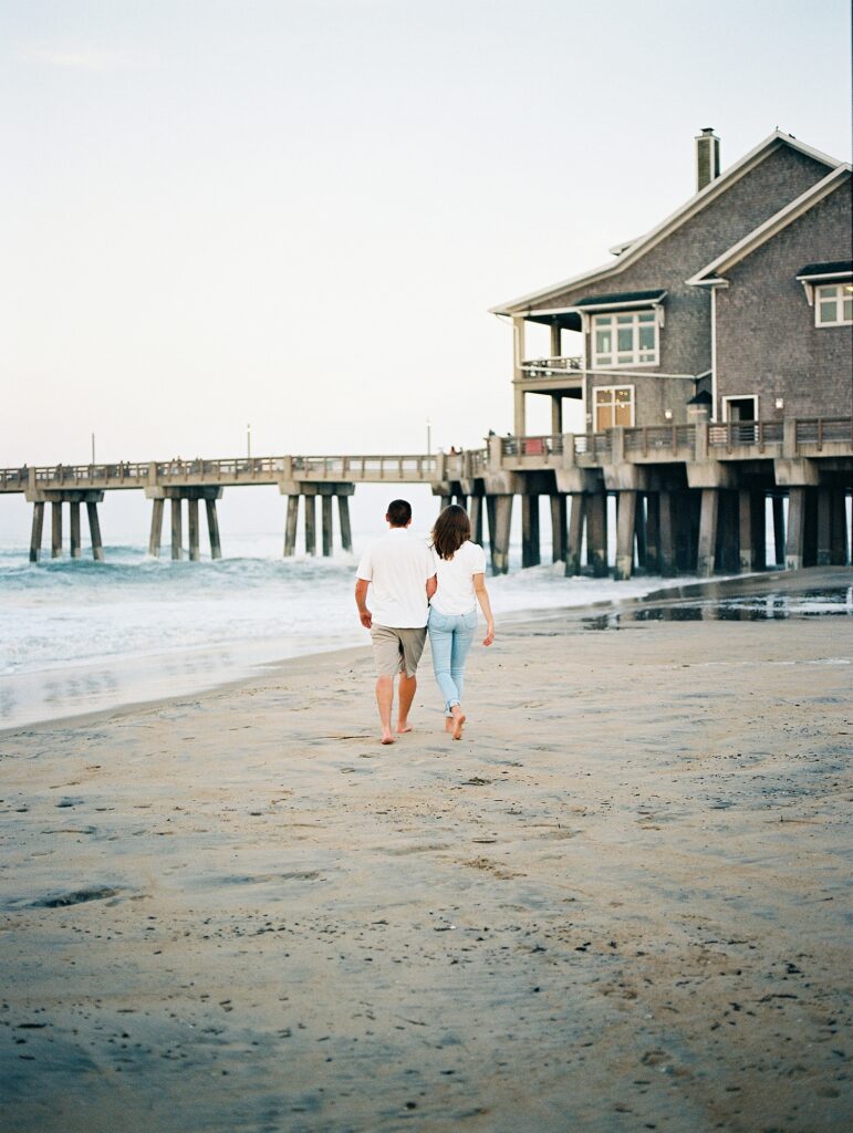 couple walk toward a pier on a New England beach