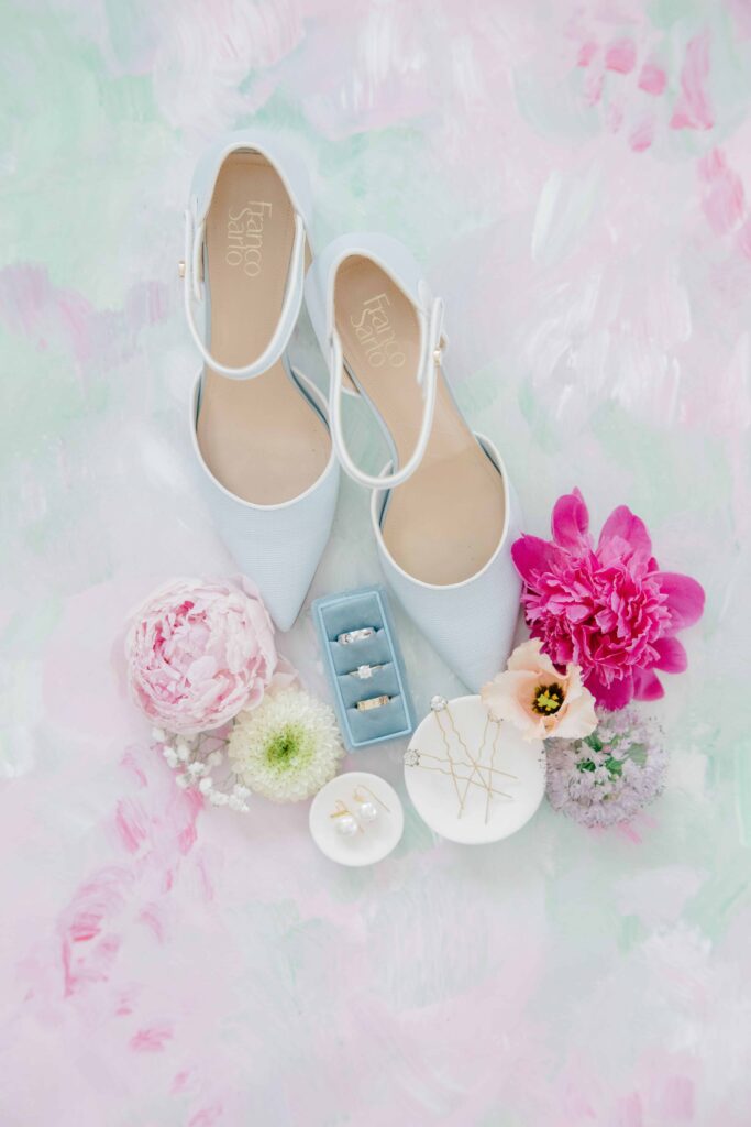 Bridal shoes, ring boxes, and vibrant pink flowers are arranged in a romantic flat lay with soft pastel tones. Thoughtfully styled wedding details for an Aldworth Manor wedding.