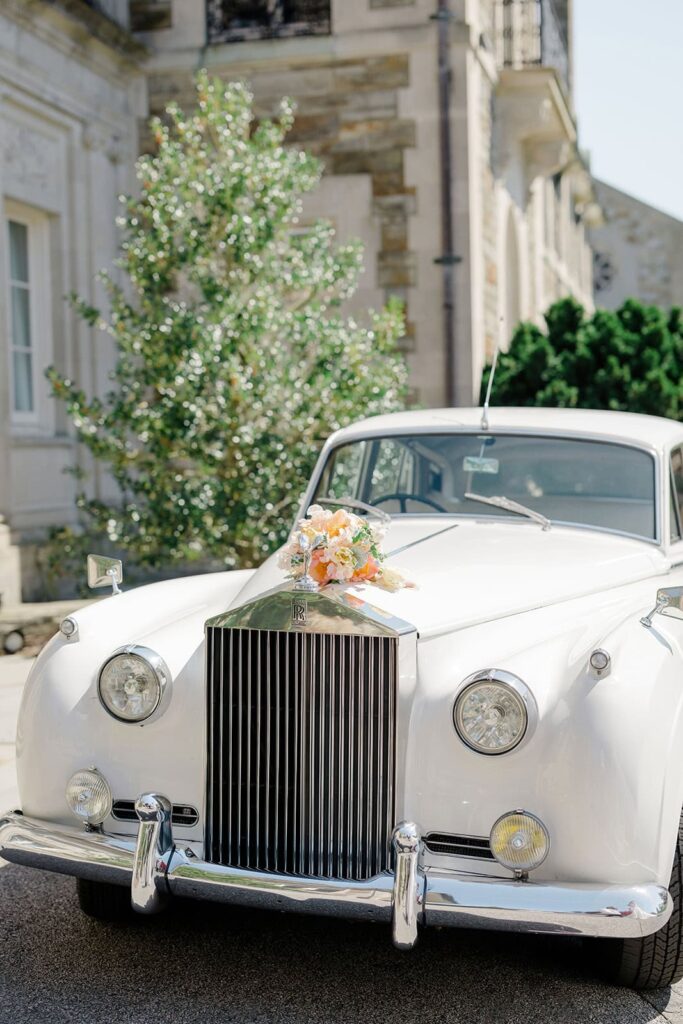 A vintage Rolls-Royce with a floral bouquet on the hood is parked outside the estate, adding classic character to a New England wedding venue.