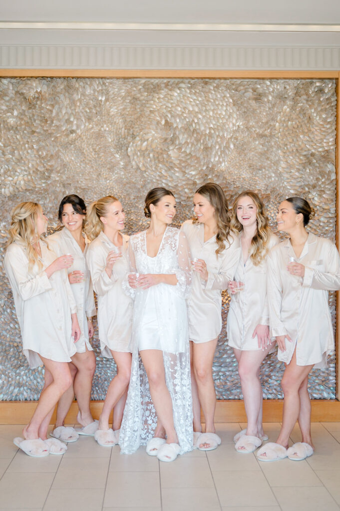Candid bridal party getting ready moment at Belle Mer, with bride in lace robe surrounded by bridesmaids in satin pajamas.