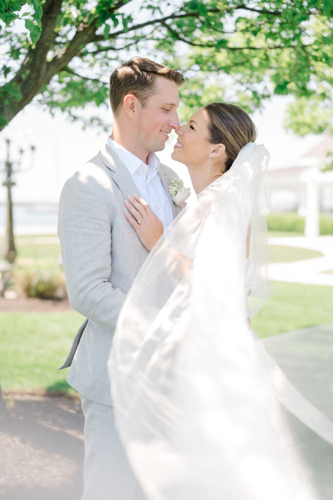 Bride and groom embracing during waterfront first look at Belle Mer, veil flowing in the breeze.