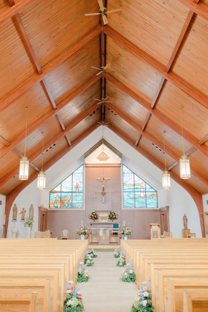 Interior view of church ceremony space with wooden beams and floral-lined aisle for Belle Mer wedding in Newport, Rhode Island.