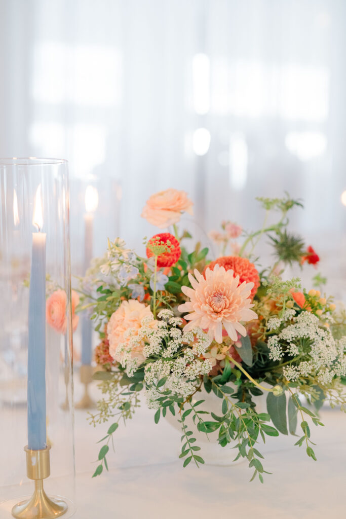 Close-up of colorful Belle Mer wedding centerpiece with peach blooms and blue taper candles.