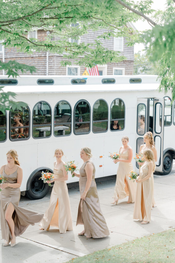 Bridesmaids in champagne and bronze dresses stepping off white trolley with bouquets in hand for Belle Mer wedding.