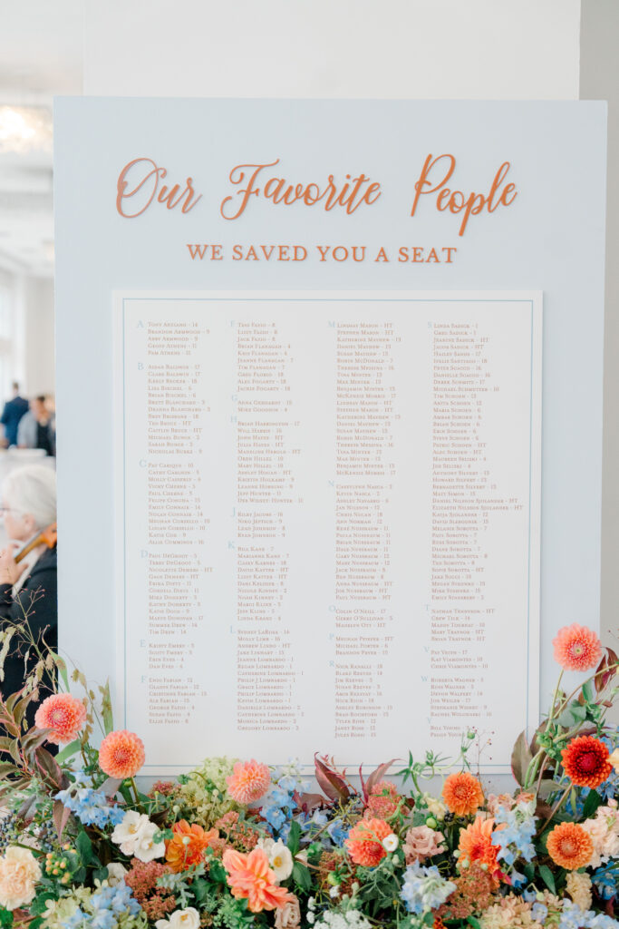 Close-up of Belle Mer wedding seating chart with orange and peach florals for coastal autumn wedding reception.