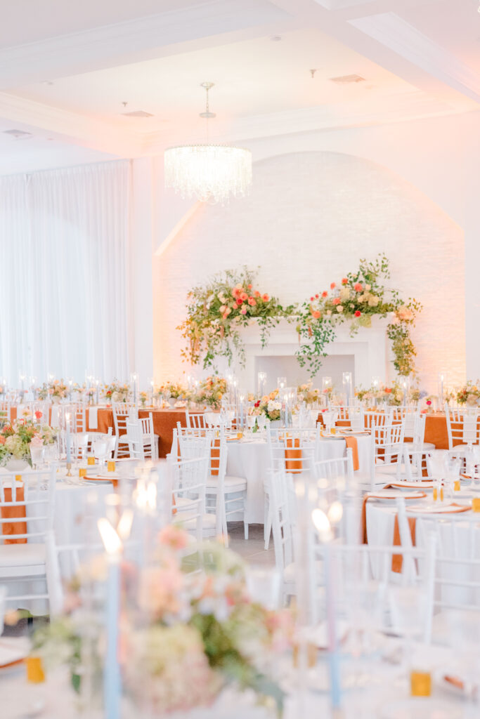 Reception room view with autumn floral decor and orange linens at Belle Mer wedding.