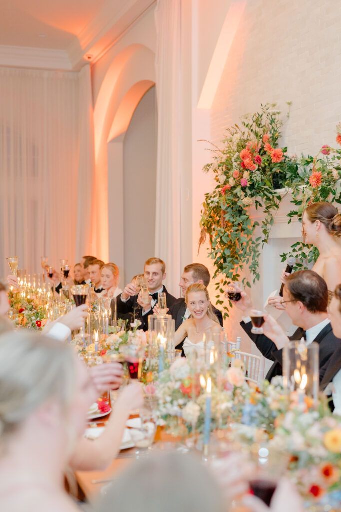 Bride and groom toasting with wedding guests at Belle Mer reception head table with candlelit decor.
