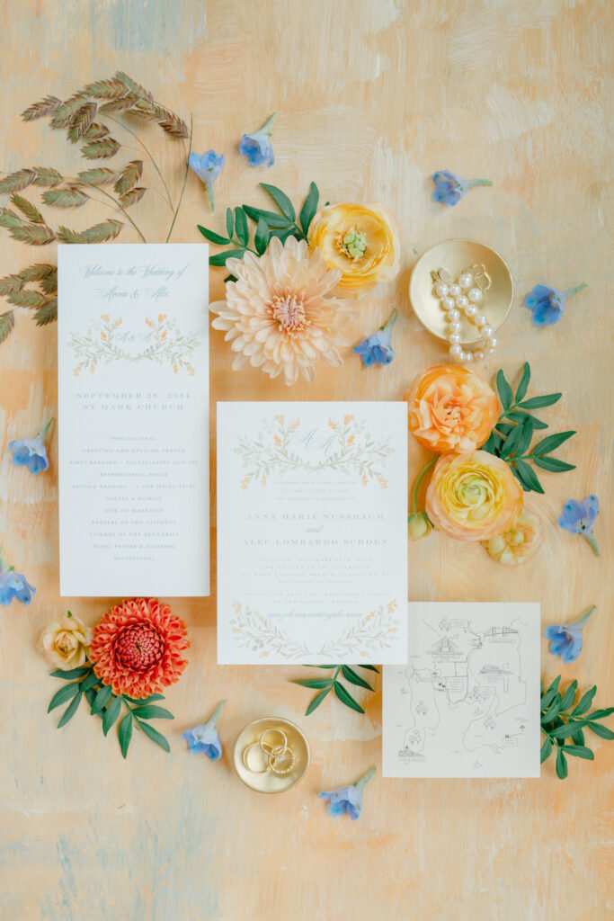 Elegant flatlay of Belle Mer wedding details featuring invitation suite, bridal shoes, wedding rings, Chanel perfume, and vibrant floral accents.