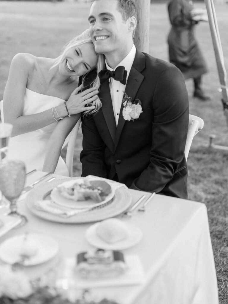 Candid reception moment of guests dining beneath sailcloth tent by the water.