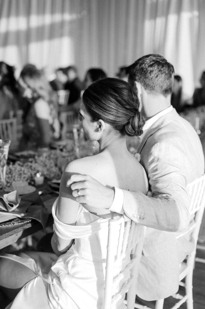Candid black and white photo of bride and groom seated at their Belle Mer wedding reception in Newport, Rhode Island.