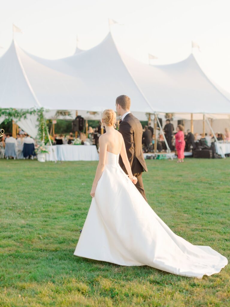 Bride and groom walking along the lawn at Eisenhower House with ocean views in the background.