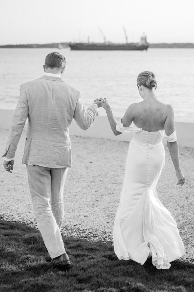 Bride and groom walking hand-in-hand along Belle Mer waterfront at sunset in Newport, Rhode Island.