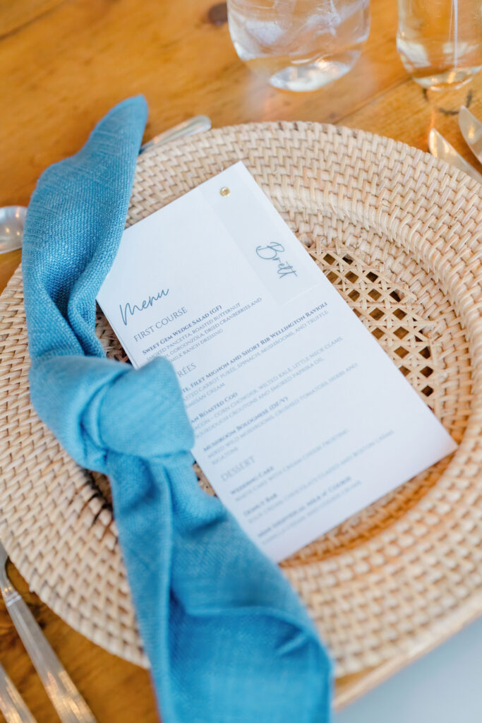 Wicker charger and blue napkin table setting at luxury Cape Cod wedding reception