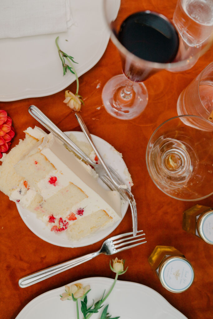 Late-night cake slice with wine glass and wedding favors on burnt orange linen at Belle Mer reception.