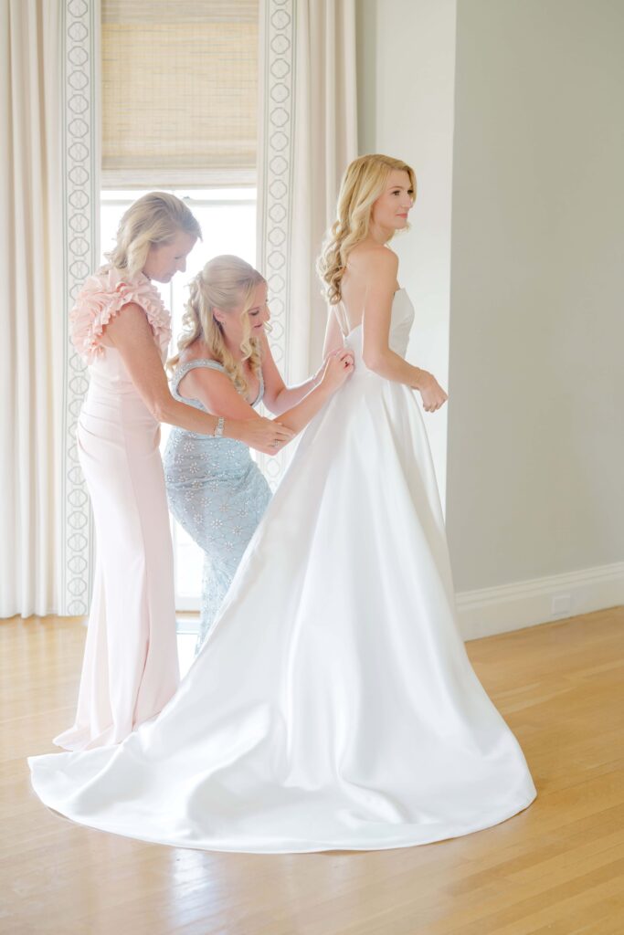 Bride preparing in bridal suite at Eisenhower House, smiling as light pours through the window.