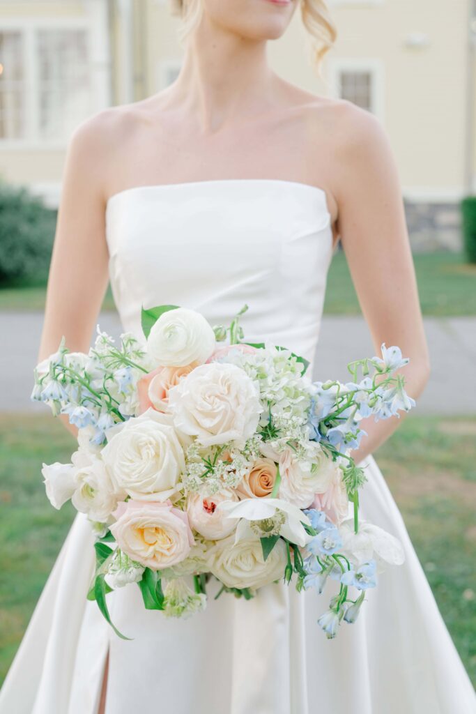 Close-up of bridesmaid holding pastel bouquet with dusty blue and peach blooms.