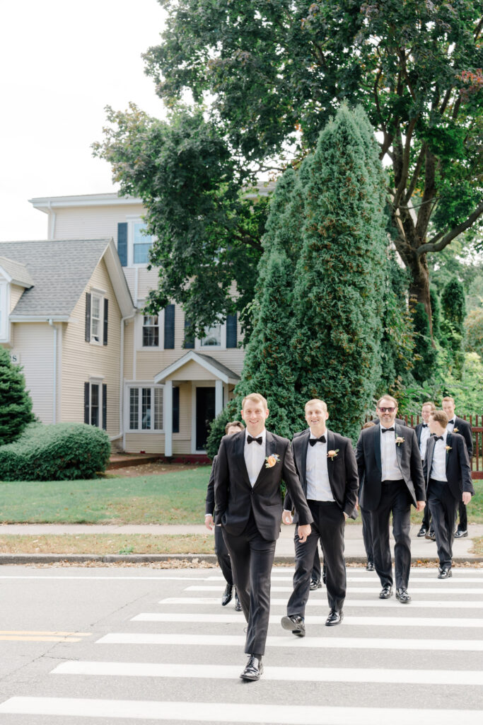 Groomsmen in black tuxedos walking across street in Newport before Belle Mer wedding ceremony.
