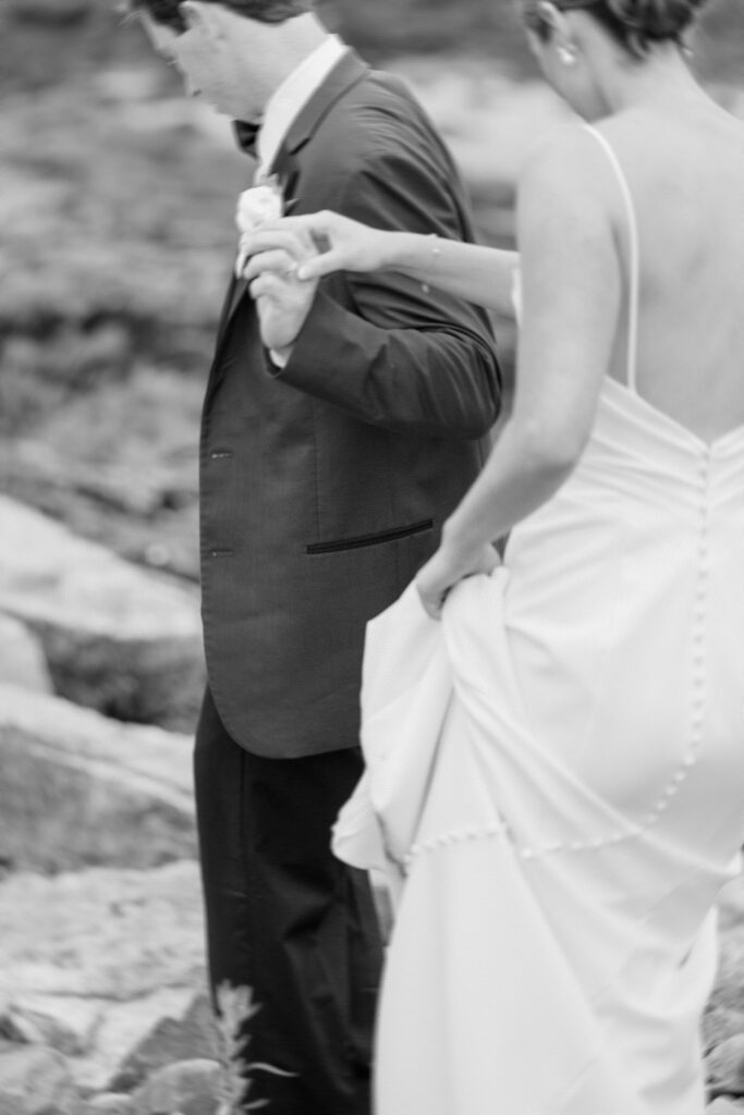 Bride and groom holding hands during intimate portraits on the rocky New Hampshire coastline.