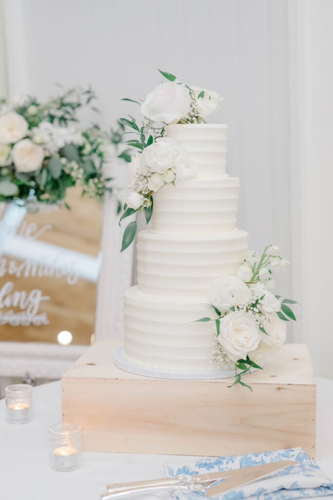 Three-tier white wedding cake decorated with fresh flowers at Wentworth by the Sea Country Club.