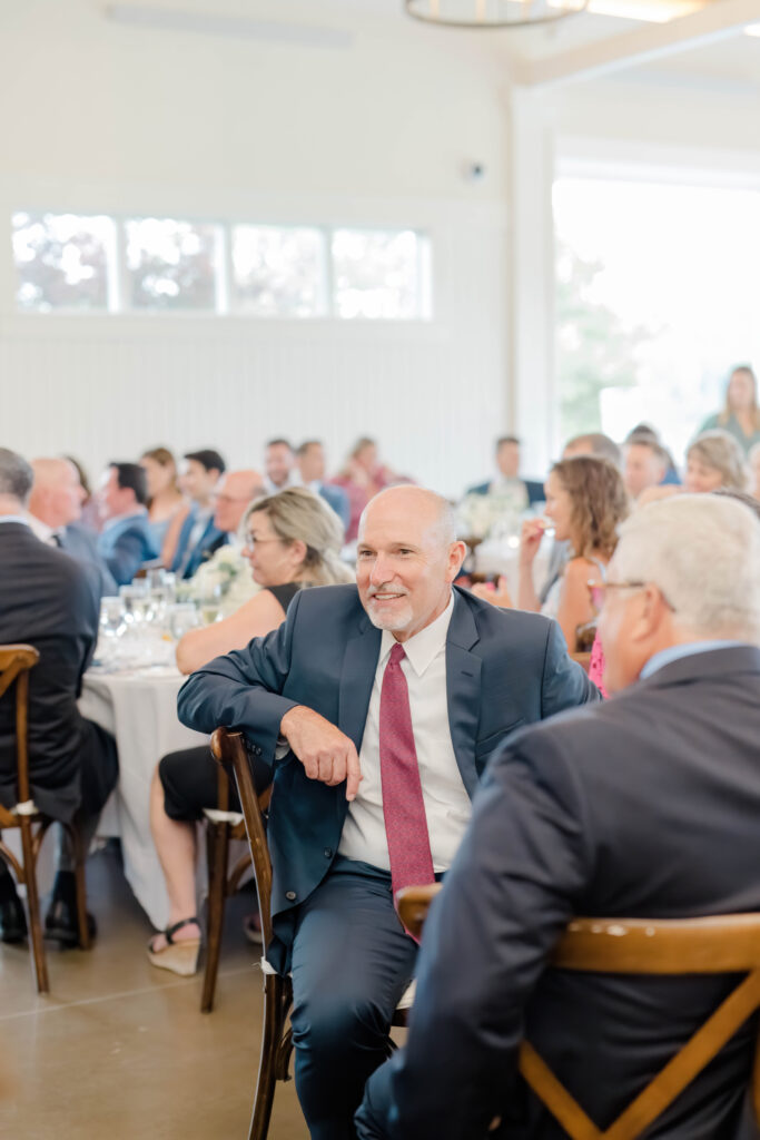 Guests smiling and reacting during heartfelt wedding toasts at the reception.