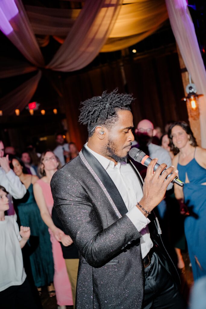 A singer moves through the dance floor with guests gathered close around him, bringing energy and celebration to this luxury barn wedding in New England.