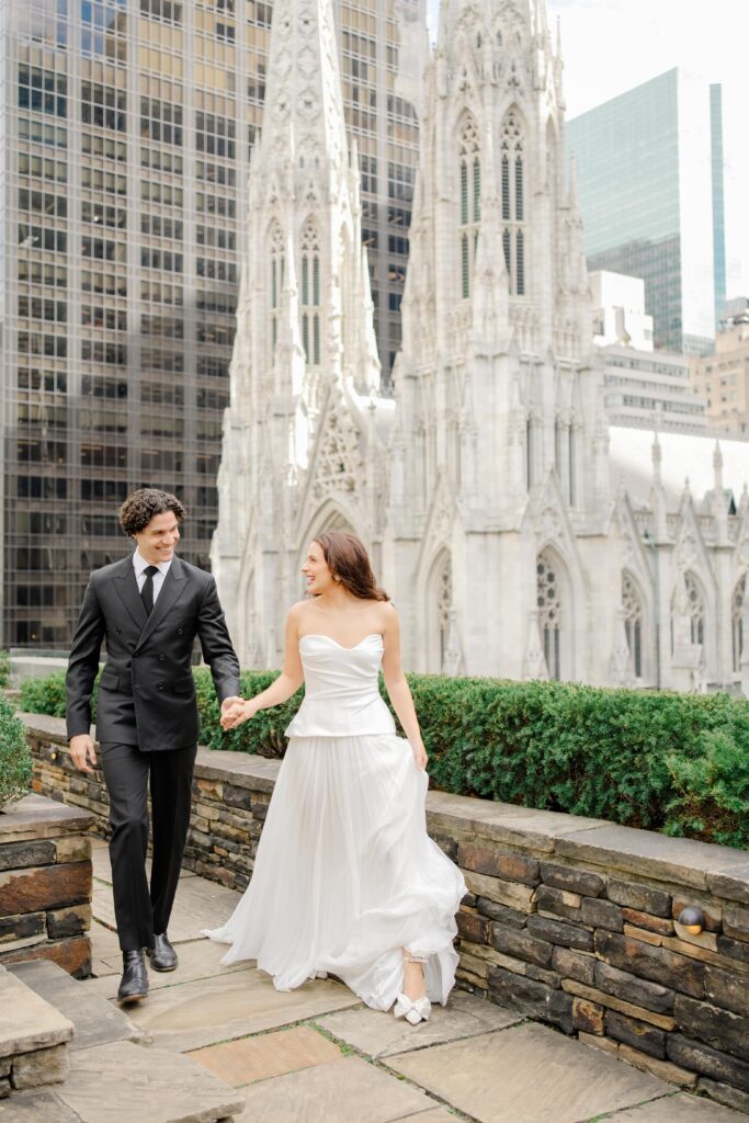 The bride and groom stroll together beside the cathedral, blending historic architecture with the energy of Manhattan. A signature scene from a 620 Loft and Garden wedding ceremony.