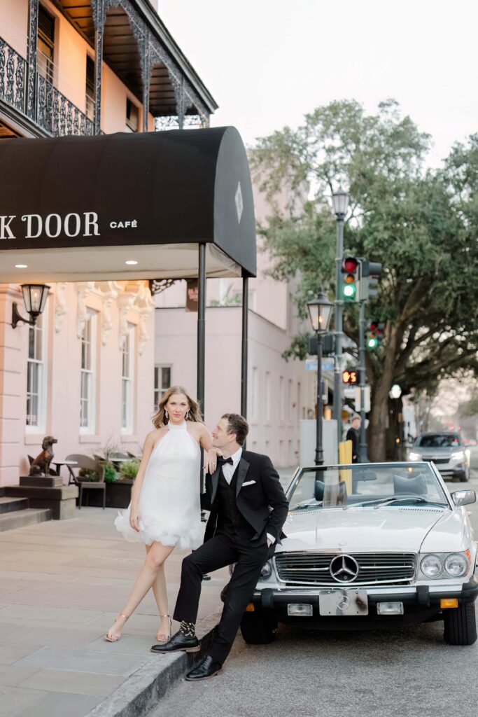 Stunning couple posing with a white vintage Mercedes in front of The Black Door Café on Meeting Street in downtown Charleston SC at golden hour