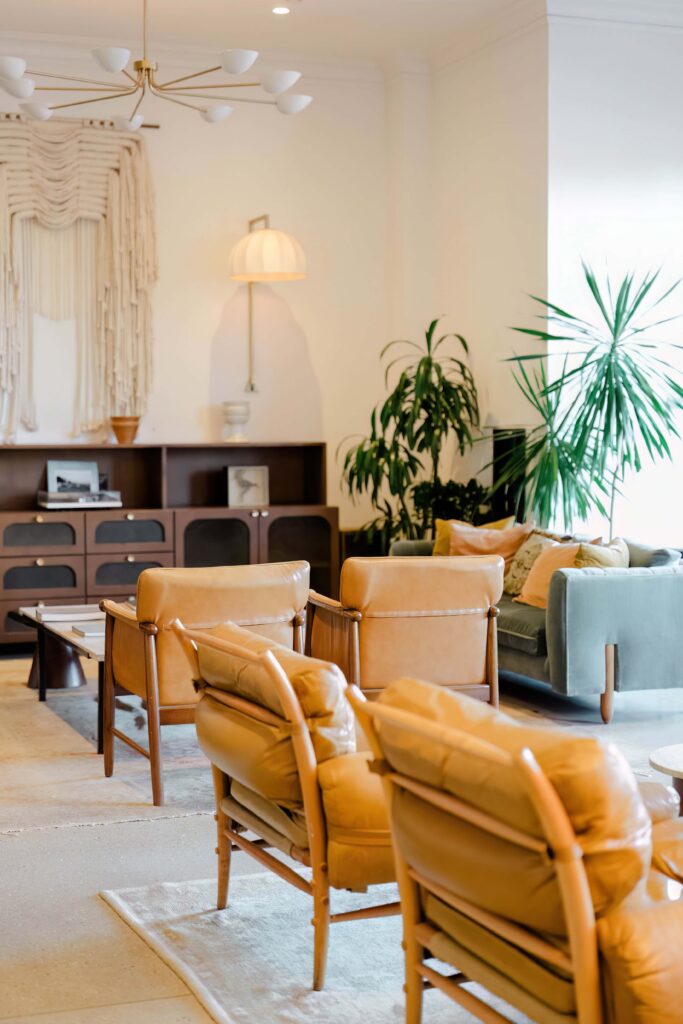 Beautiful boho-luxe lobby interior at a boutique hotel in downtown Charleston SC — caramel leather chairs, brass chandelier, macrame wall art and tropical plants