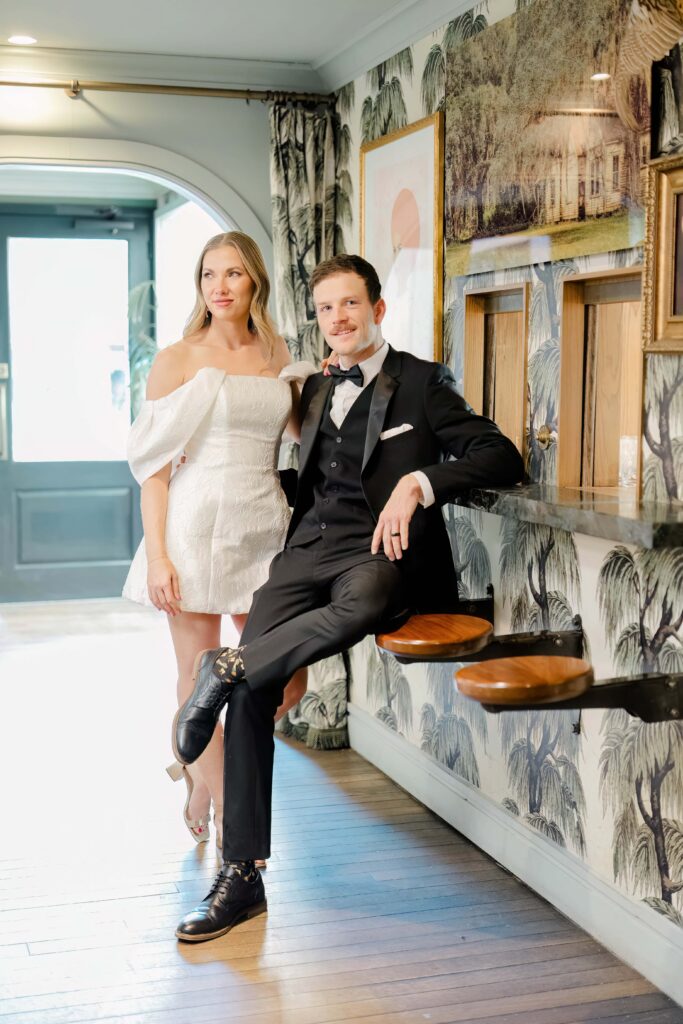 Laughing couple standing together at a warm wood bar in a downtown Charleston SC hotel during a stylish couples session — Felisha Lees Photography