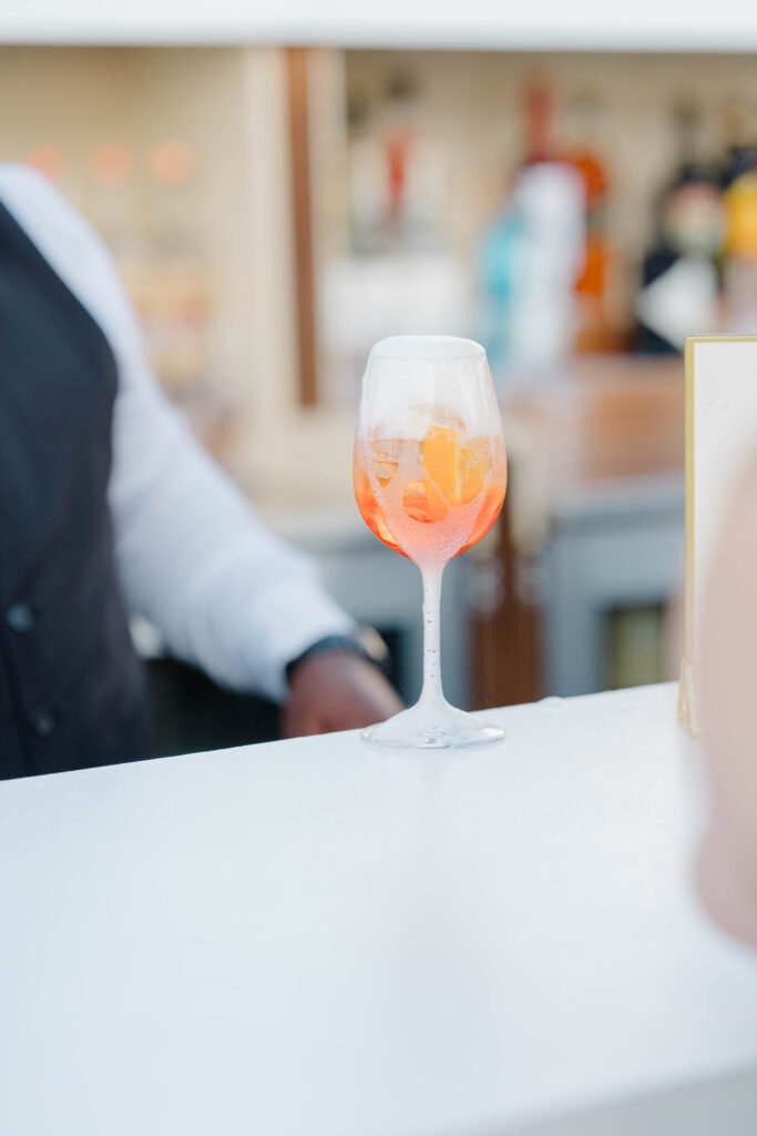 A signature cocktail rests on a reception table as soft afternoon light filters through the venue. Elegant reception details from a luxury Castle Hill Inn wedding.