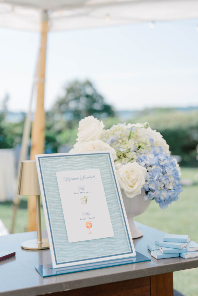 A thoughtfully styled welcome display featuring blue hydrangeas, elegant stationery, and coastal-inspired details greets arriving guests. Fine-art wedding details from a Castle Hill Inn wedding celebration.