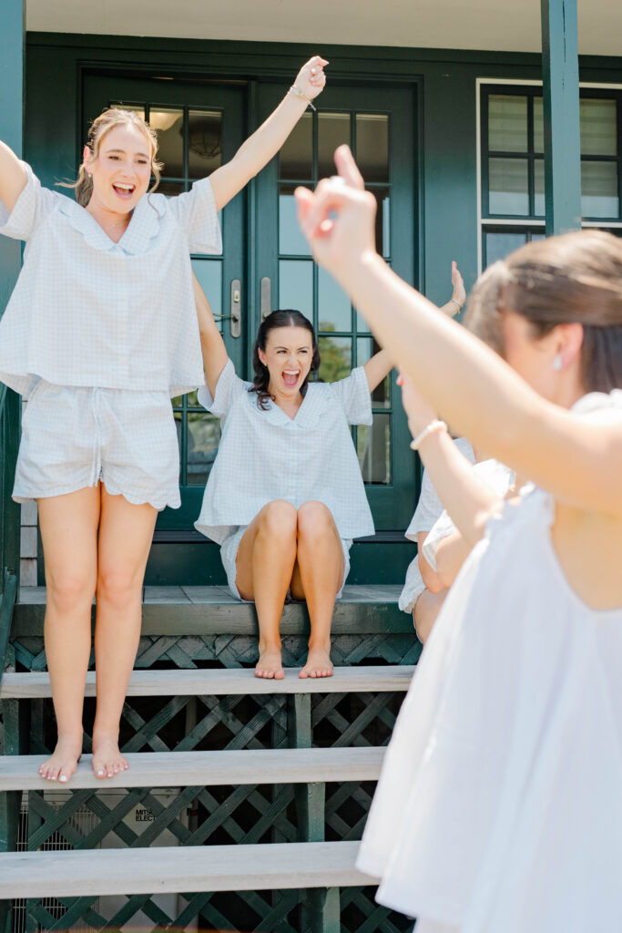 Bridesmaids cheer from the cottage steps while celebrating together before the ceremony with genuine excitement and laughter. A memorable getting-ready moment at a Castle Hill Inn wedding.