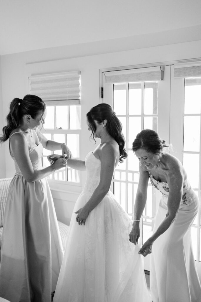 A bride shares a quiet getting-ready moment with her loved ones as they help with the final touches before the ceremony. An elegant beginning to a luxury celebration when planning a Castle Hill Inn wedding cost.