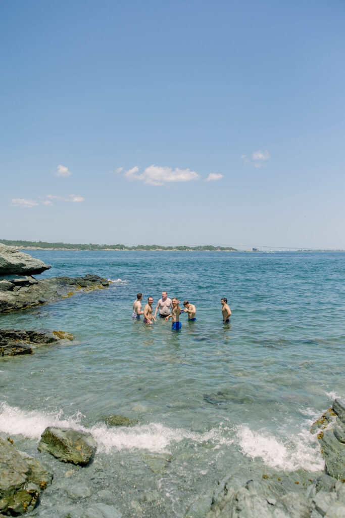 Wedding guests laugh and splash together in the ocean after the celebration, creating an unforgettable candid moment by the water. A joyful tradition often seen during a Castle Hill Inn wedding.